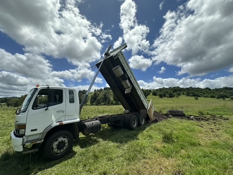 Dump truck unloading dirt in green field, symbolizing Stone & Rubble's acreage mowing and property maintenance services.